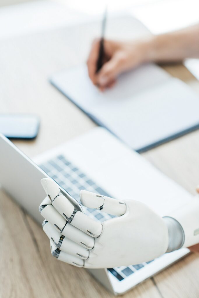 Roboterhand hält Bildschirm und im Hintergrund schreibt eine Hand in einen Block. - Symbolbild für die AI Masterclass.